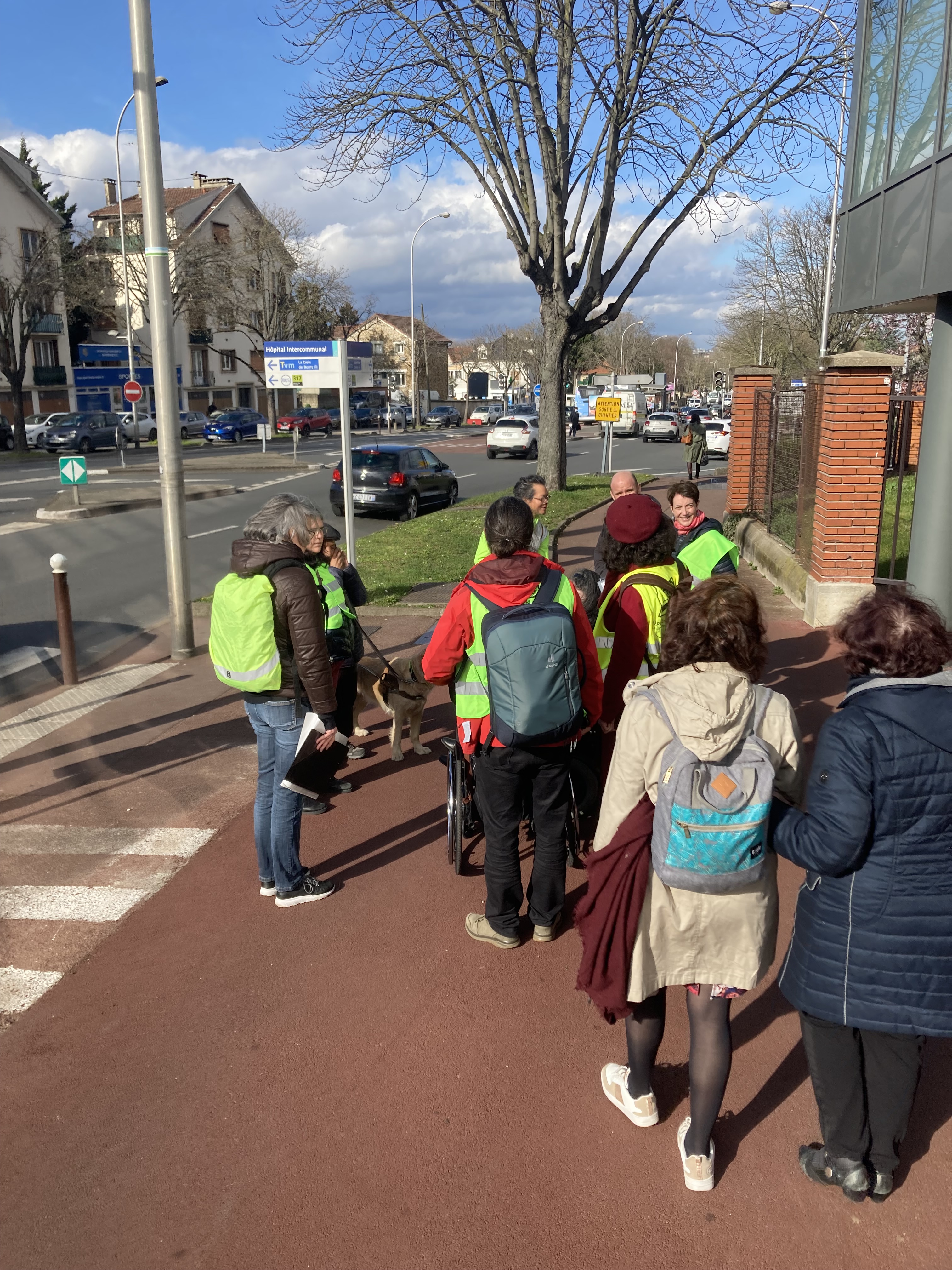 Un petit groupe de personnes, certaines portant des chasubles jaune fluo, discutent sur le trottoir de l'avenue de Verdun à Créteil
