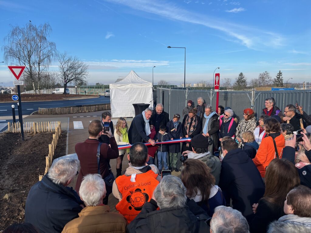 Vue d'un important groupe d personnes (des dizaines) de dos, devant des élus et des enfants souriants, le ruban bleu-blanc-rouge va être coupé. Des gens prennent des photos.